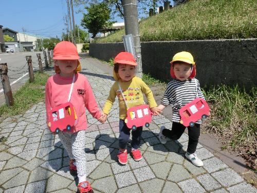 写真：自分たちで制作したお弁当をモチーフにしたバス型のバッグを下げて、手をつないでお散歩する2歳児ぱんだ組の子どもたち