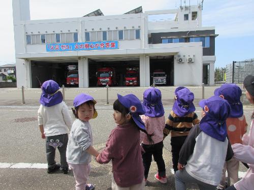 写真：近くの消防署へお散歩に来た2歳児こあら組の子どもたち。3台の消防車と1台の救急車を歩道から眺めています