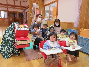 写真：0歳児と1歳児が段ボールでできた獅子舞と一緒に写真を撮っているところ