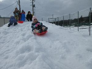 女の子が雪山でソリ滑りをしている写真
