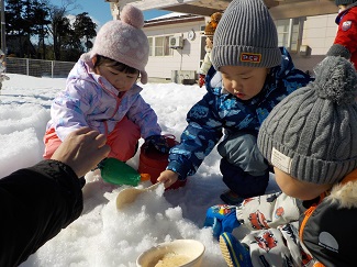 写真：0・1歳児の子ども達がお皿やスコップで雪遊びを楽しんでいる様子