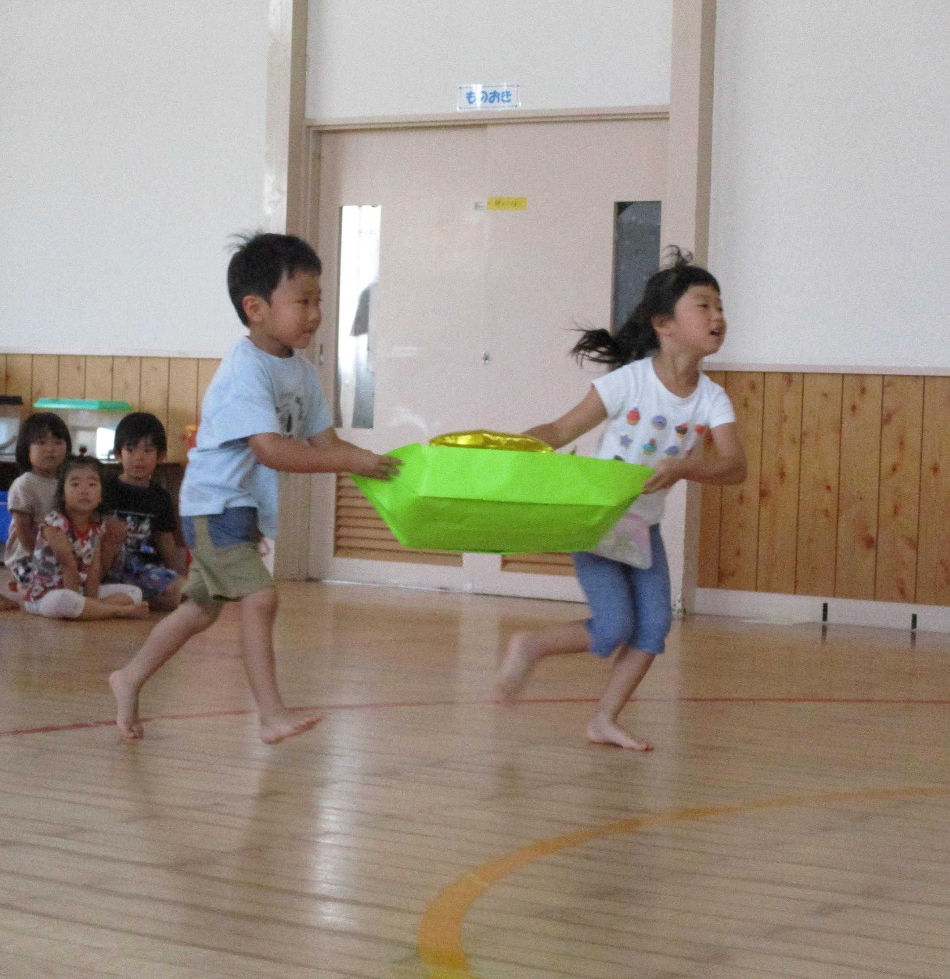 写真：2人の園児が笹船に見立てた箱に星の飾りを乗せ、落とさないように協力して走っています