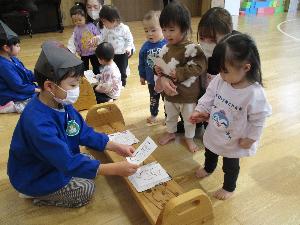 写真：郵便屋さん役の年長児が0・1歳児のお友達にハガキを渡しています