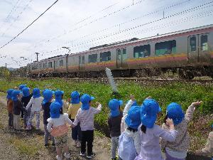 写真：青い帽子をかぶった園児が、散歩中に走りすぎる電車に手を振っています