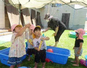 写真：うさぎ組の2歳児が水鉄砲や霧吹きを上に向けて水を出して遊んでいます