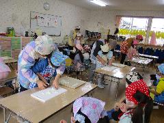 写真：年長児が保育士と一緒に、おでんに入れる具材を包丁で切っています。