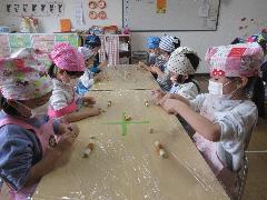 写真：年中児が保育室で席に座り、ちくわをちぎっています。