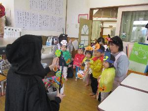 写真：黒いフード付きのマントをかぶった魔女役の職員から、折り紙のキャンディーをもらうひよこ組の1歳児