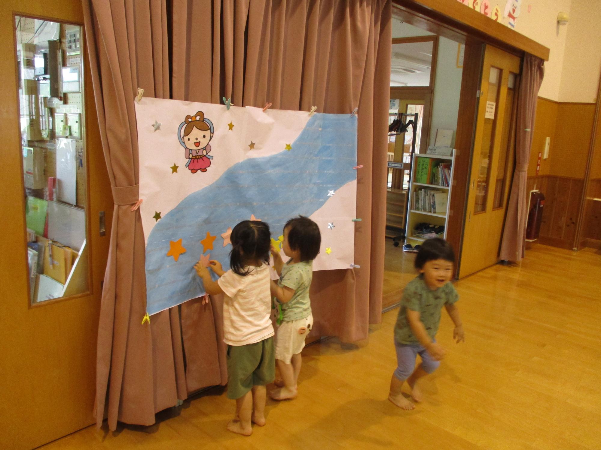 写真：天の川と織姫が描かれたポスターに、星型のカードを貼る2歳児