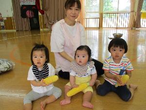 写真：皮をむいたとうもろこしを持って座っているひよこ組の女の子3人