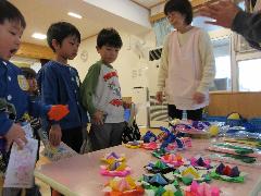 写真：机の上に並べられたカラフルなコマやおもちゃなどの景品を前に悩む3人の園児