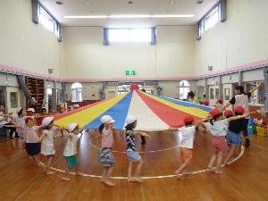 写真：遊戯室で運動会に向けてパラバルーンの練習をする3～5歳児