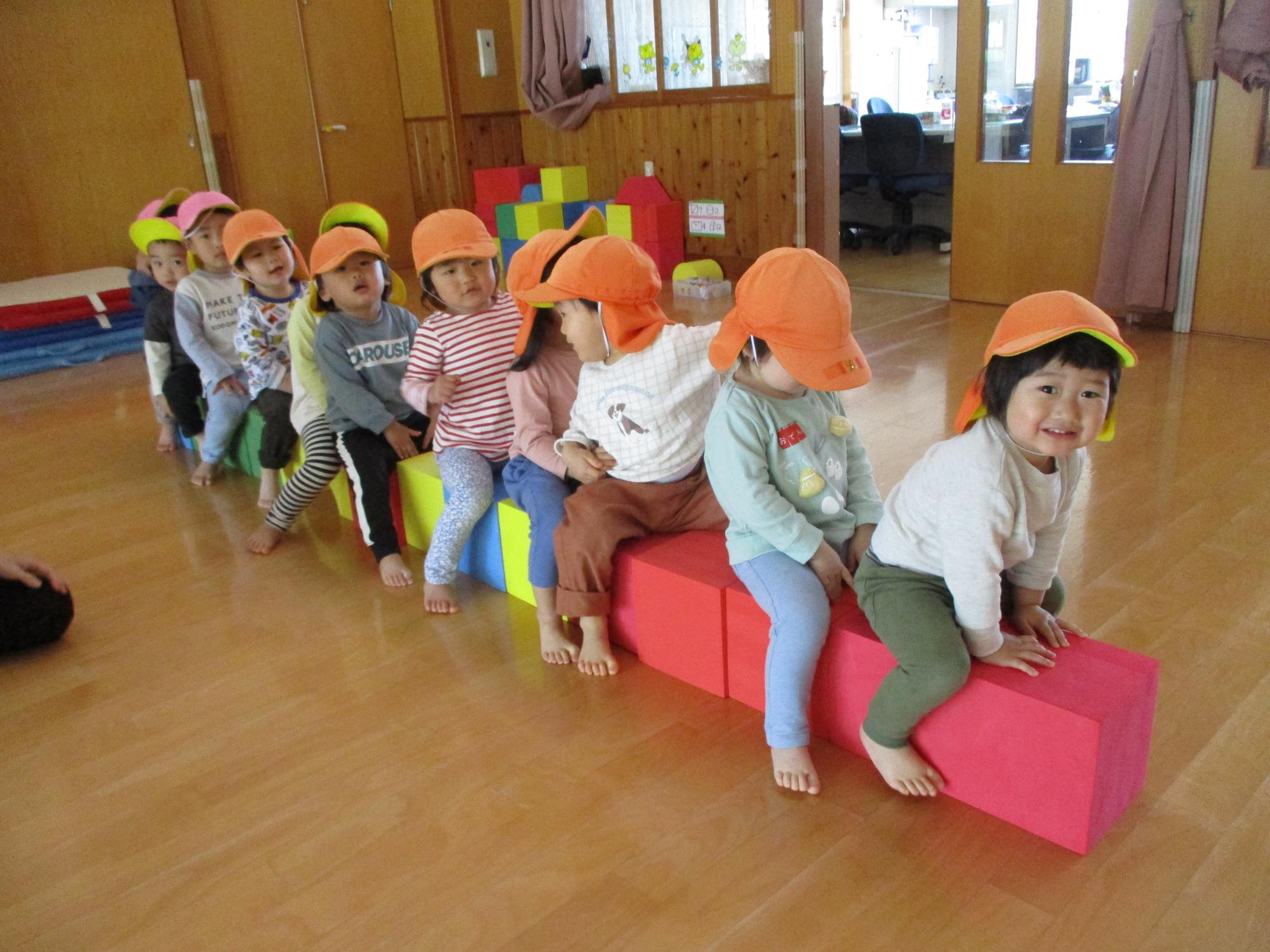 写真：うさぎ組の子どもたちが、遊戯室で大型ブロックを並べてまたがり、バスごっこをしています