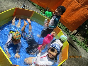写真：プールの中でワニ歩きをしたりジョウロやペットボトルで水遊びを楽しむ5人の子ども達