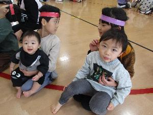 写真：年長児の膝の上に座る0歳児男児と2歳児男児。嬉しそうな表情をしています