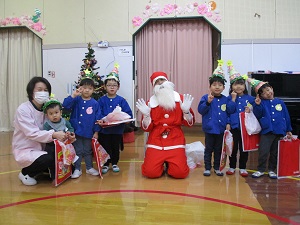 写真：サンタさんを中心に、プレゼントの袋をもって、嬉しそうな様子の子どもとの集合写真