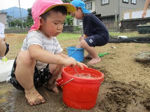 写真：3歳児がバケツの泥水をかき混ぜて遊んでいる様子