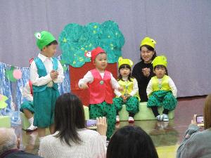 写真：かえるのお面をかぶり、ベストや緑のズボンなどの衣装をつけた子どもたちが劇を演じています
