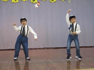 写真：黒い帽子と黒ネクタイ、サスペンダー付きのズボンの衣装で、男の子2人が踊っています