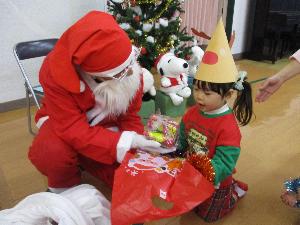 写真：クリスマスプレゼントをサンタさんから手渡され、嬉しそうな2歳児