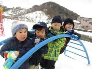 写真：雪で地面が高くなり、いつもはぶら下がって遊ぶ太鼓橋から顔を出して電車ごっこをしている子どもたち
