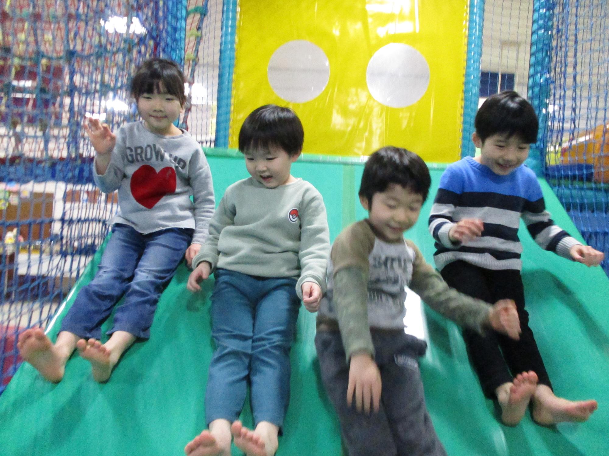 写真：横並びで滑り台を滑り降りる4人の子どもたち