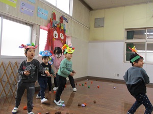写真：色とりどりの鬼のお面を被った子どもたちが、紙のボールを鬼に向かって投げているところ