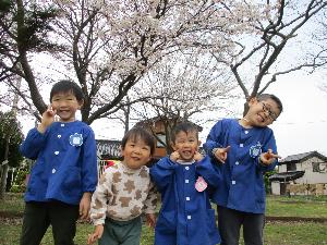 写真：小学校の校庭に咲く桜の木の下で4人並んで記念撮影をする様子