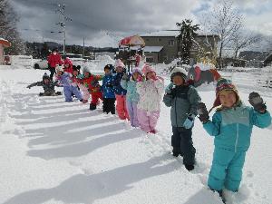 写真：今年初めての雪遊びの日に、一列に並んで、園庭に道をつけている4歳児