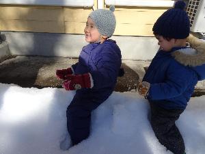 雪を電車に見立てて上にまたがり、電車ごっこをしている1歳児2名