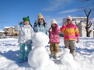 自分たちで作った大きな雪だるまと一緒にピースをしている4人の4・5歳児