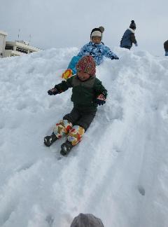 写真：子ども達が園庭の雪山を座って滑って遊んでいるところ
