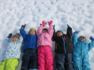 子ども達が雪の上で気持ち良さそうに両手を挙げて寝転んでいる写真