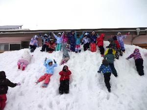 写真：5歳児の子ども達が園舎の屋根に届きそうな高さの雪山に登っているところ