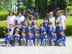 3歳児の子どもたちと保育者が公園で整列しポーズをとっています。