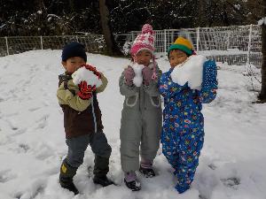 写真：雪の塊を持ってポーズをとっている3人の子どもたち