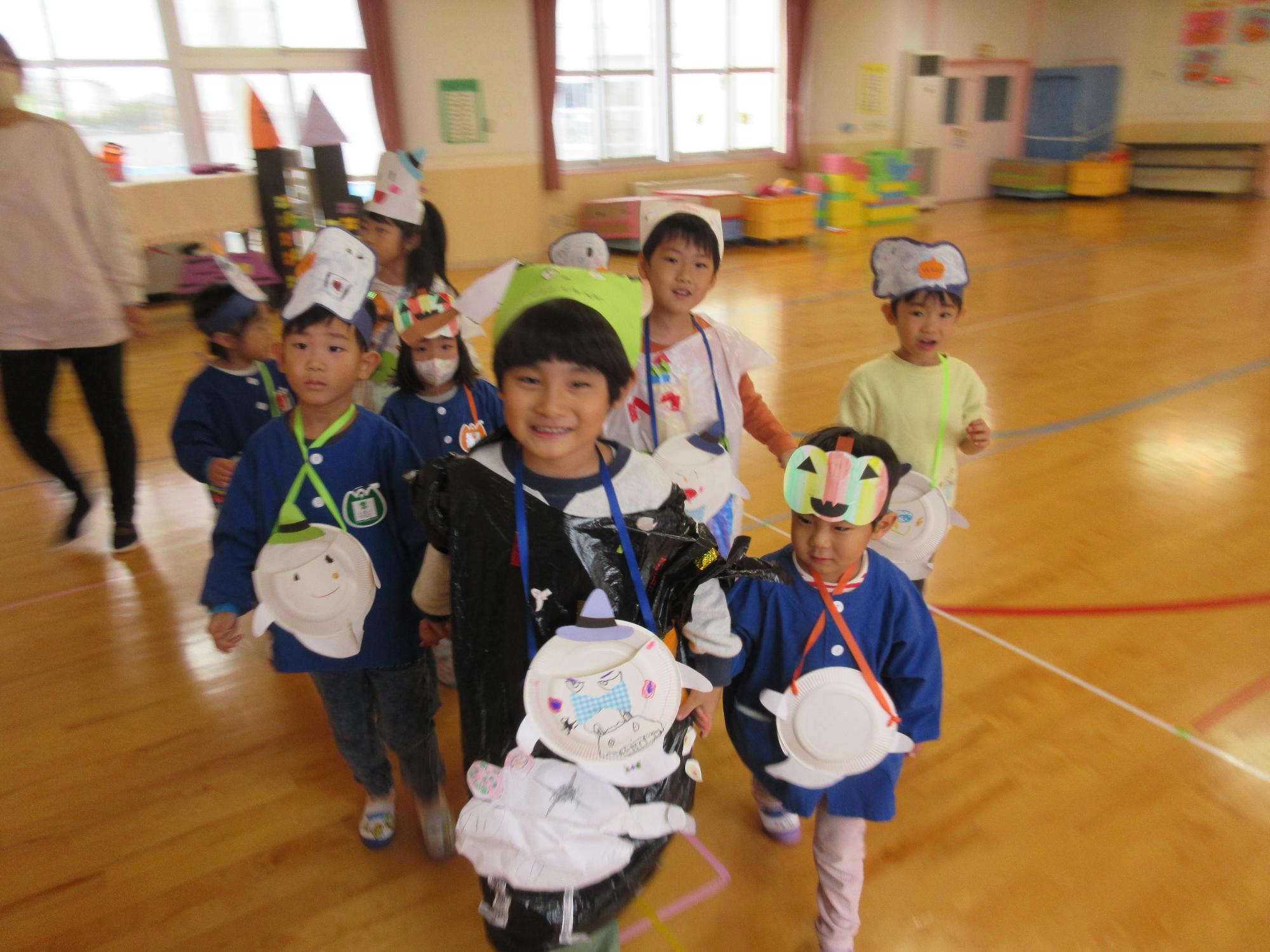 写真：2人1組で手をつなぎ、遊戯室を出発しようとする3～5歳児のチーム