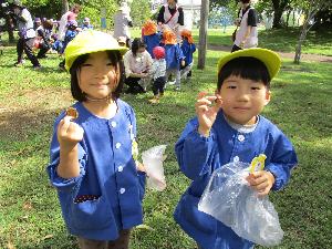 写真：芝生の広場で拾ったどんぐりを見せてくれる男の子と女の子