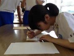 定規と鉛筆を使って白い紙をゲームで定められた大きさに切っている生徒の写真
