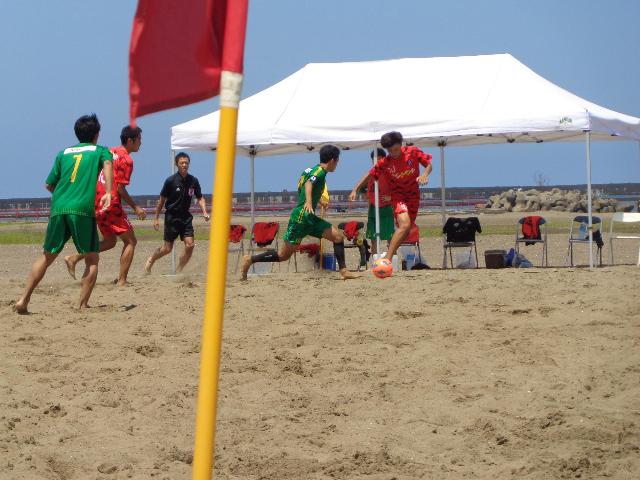 赤色と緑色のユニフォームを着た選手がビーチサッカーを行っている様子