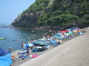 緑の山に囲まれた美しい景観の海辺でたくさんの人が楽しむ穴場な上輪海水浴場の写真