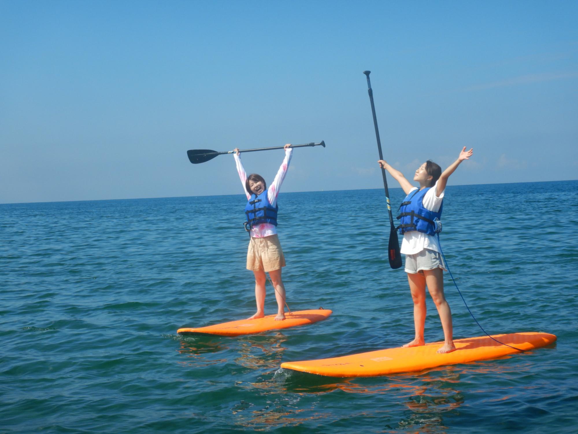 写真：海に浮かぶSUPボードの上で、両手を広げる2人の女性