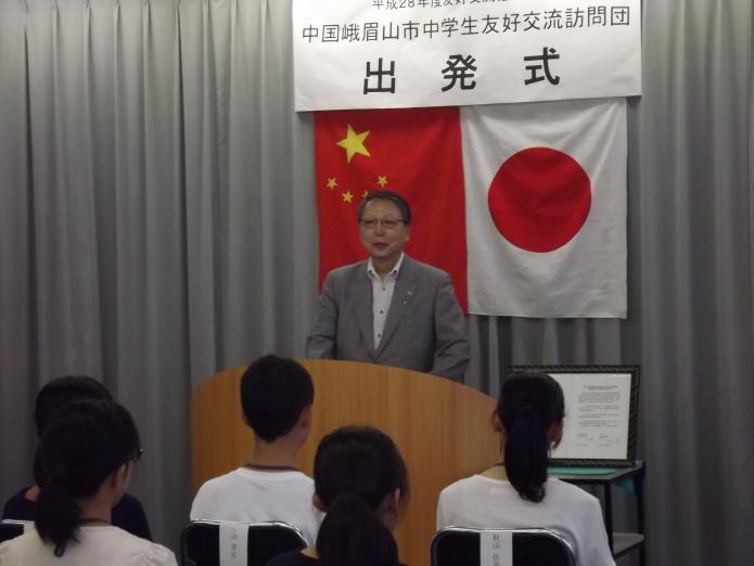 中国と日本の国旗の前で訪問団を激励する会田市長の写真