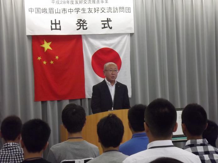 中国と日本の国旗の前であいさつをする団長の本間教育長の写真
