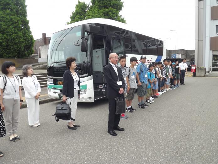出発前の訪問団員の皆さんがバスの前に並び、本間団長が挨拶している写真