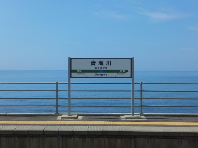 青い空、青い海、背景に日本海が広がる青海川駅ホームの駅名標の写真