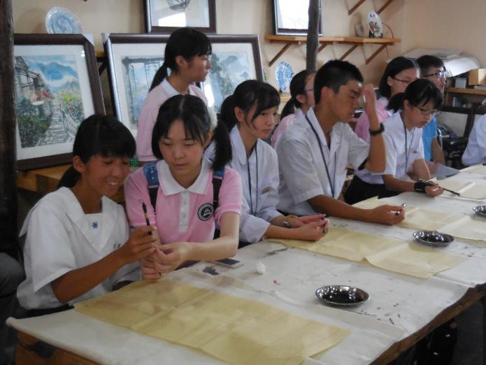 書道の授業で中国の中学生に筆の持ち方を教わっている様子の写真