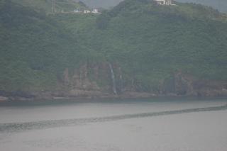 緑の中に白い滝の水が海へ流れ落ちている恋人岬から撮影した「お弁が滝」の写真