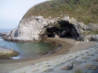 海岸に突き出た石山に大きな穴があいている鯨波鬼穴の全景の写真