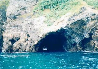 きれいなエメラルドグリーンの海と接する岸壁に大きな穴の開いた洞窟の猩々洞（しょうじょうどう）の写真